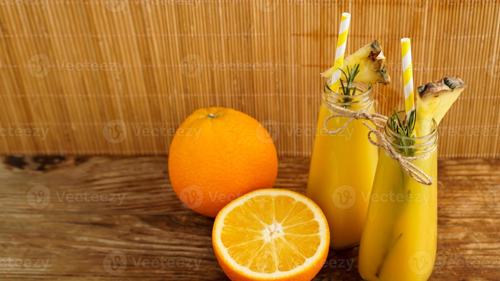 zwei Flaschen tropischer Saft mit Papierstrohhalmen. Orangen und Ananas foto