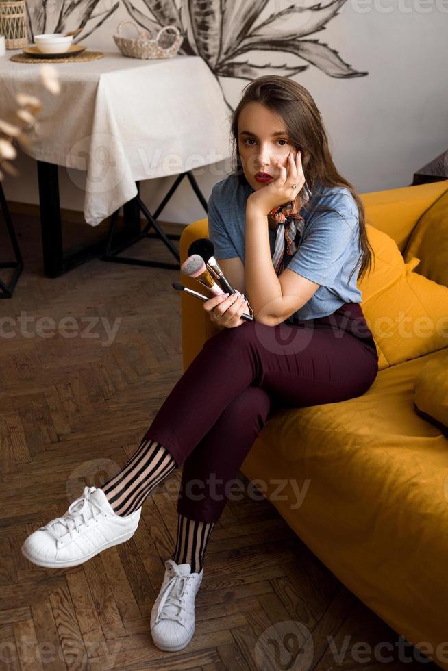 Visagistin mit Pinsel auf der Couch sitzend foto