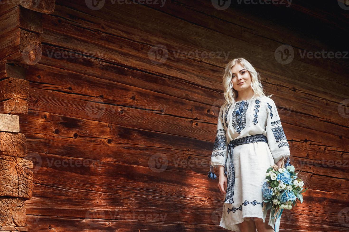 schöne Frau im bestickten Hemd in der Nähe eines Holzhauses foto