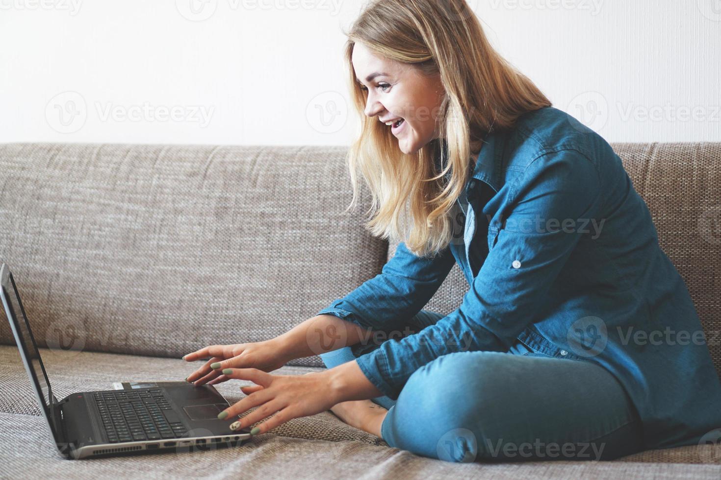 lächelnde Blondine, die sich mit ihrem Laptop auf der Couch entspannt foto