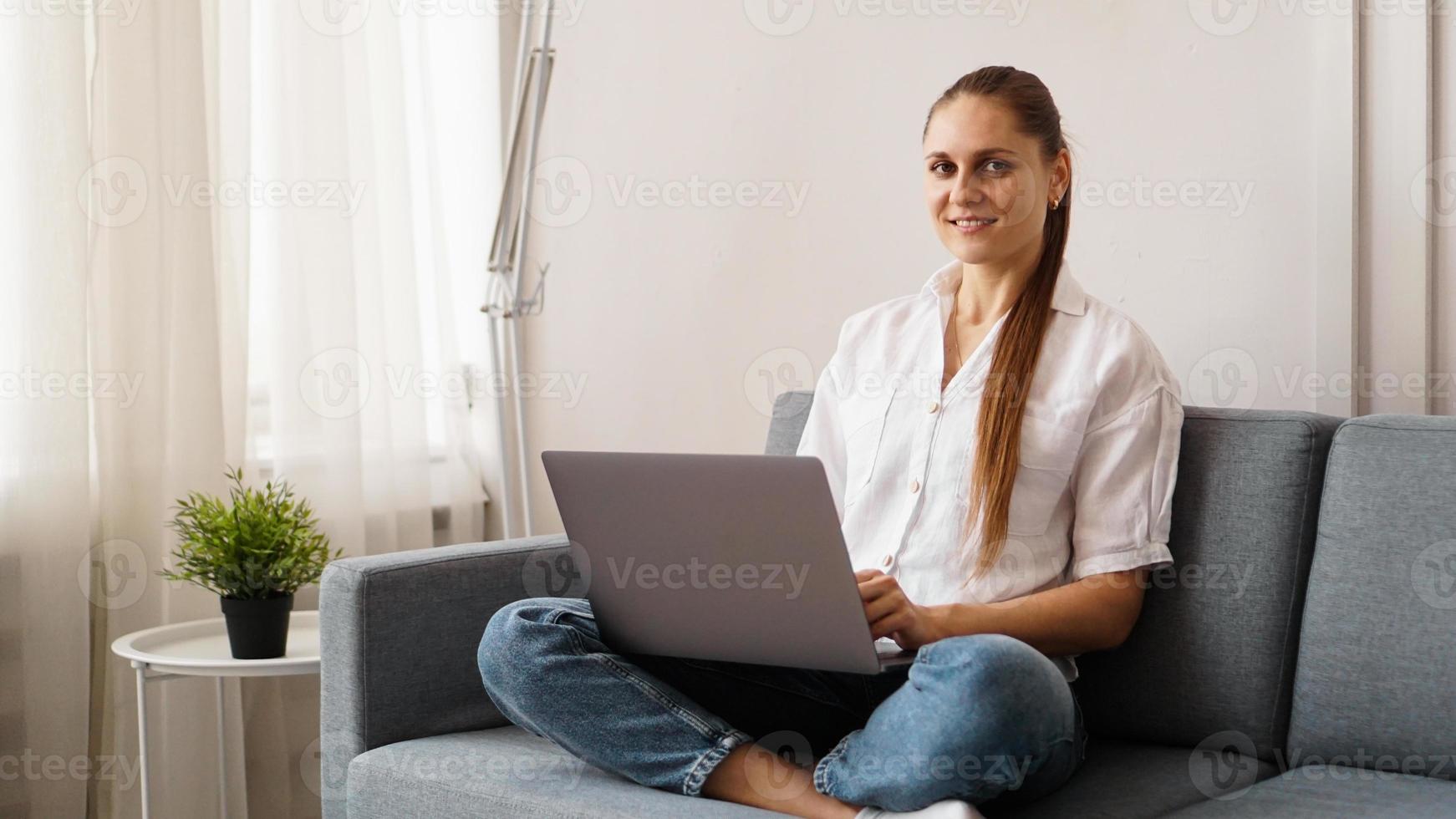 lächelnde glückliche Frau, die auf dem Sofa sitzt und Laptop benutzt foto