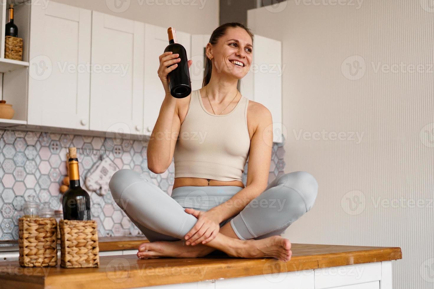 Frau im Trainingsanzug in einer hellen Küche trinkt Rotwein foto
