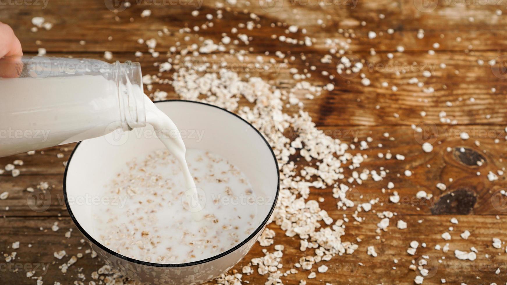 Haferflocken in eine Schüssel geben. Milch gießt in eine Schüssel auf einem hölzernen Hintergrund. foto