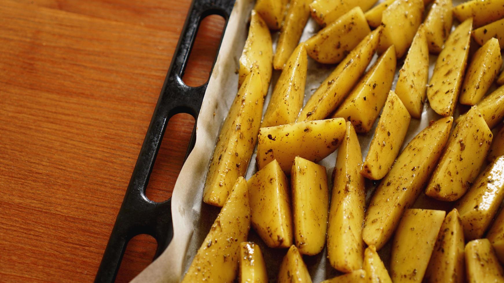 geschnittene rohe Kartoffeln auf einem Backblech mit Gewürzen foto