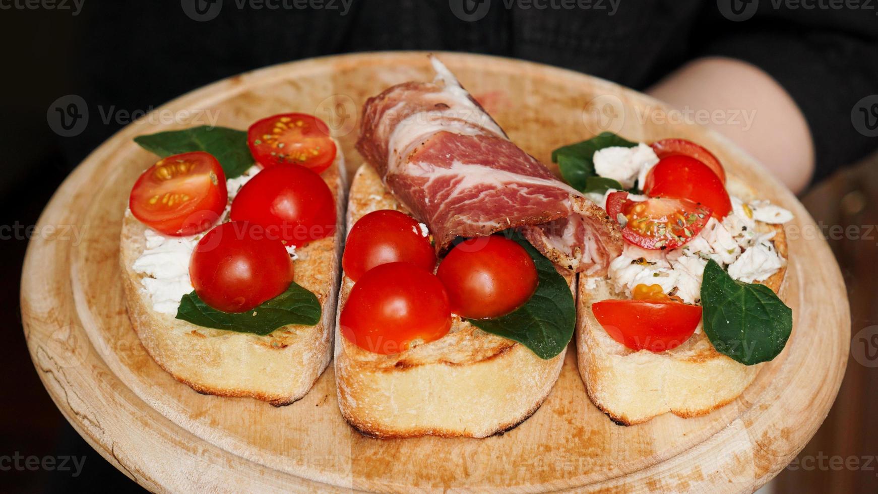 Kellnerin hält ein Holztablett mit Bruschetta in der Hand foto