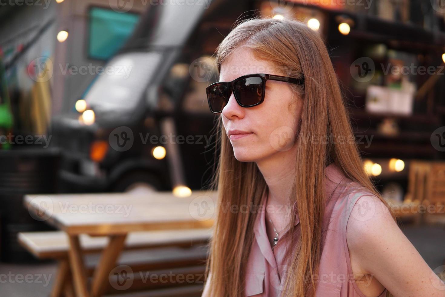 junge Frau mit Sonnenbrille auf dem Hintergrund eines schwarzen Imbisswagens foto