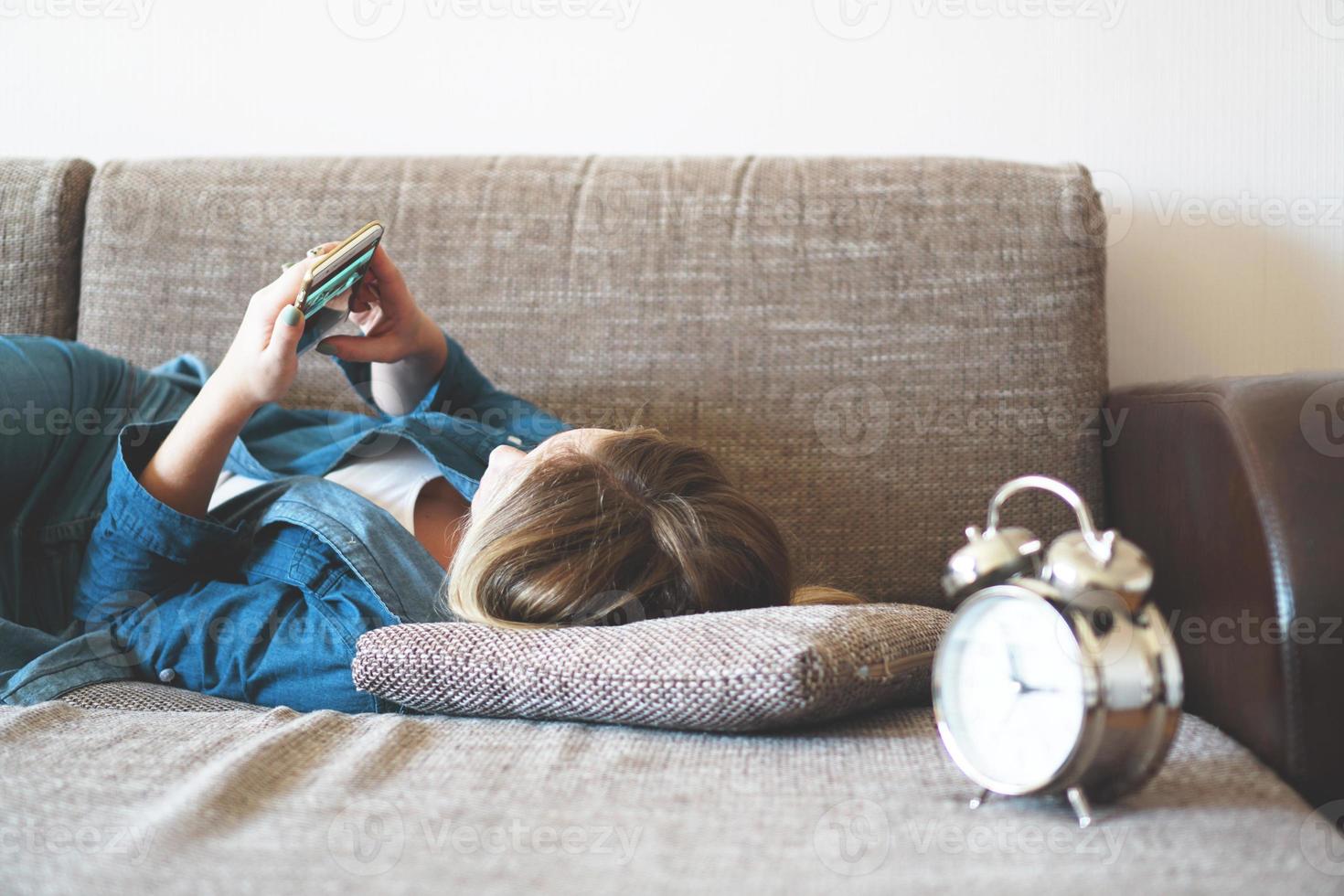 junge Frau, die im Bett telefoniert und auf den Bildschirm schaut foto