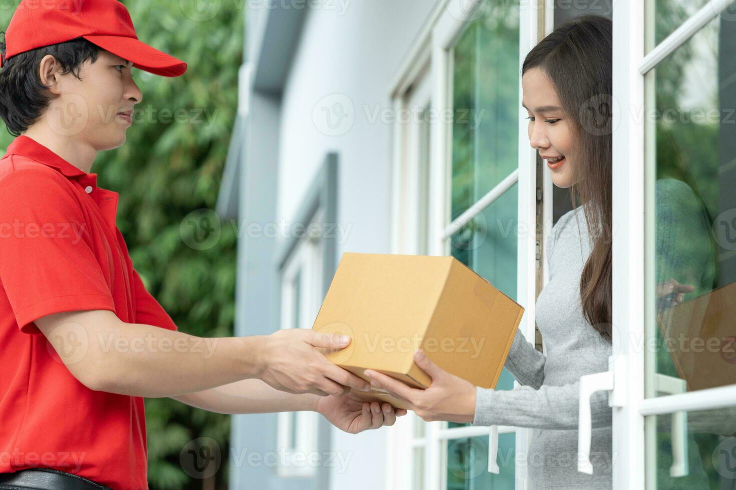 glücklich lächelnd Frau erhält Kisten Paket von Kurier im Vorderseite Haus. Lieferung Mann senden liefern äußern. online Einkaufen, Papier Behälter, wegbringen, Briefträger, Lieferung Service, Pakete foto