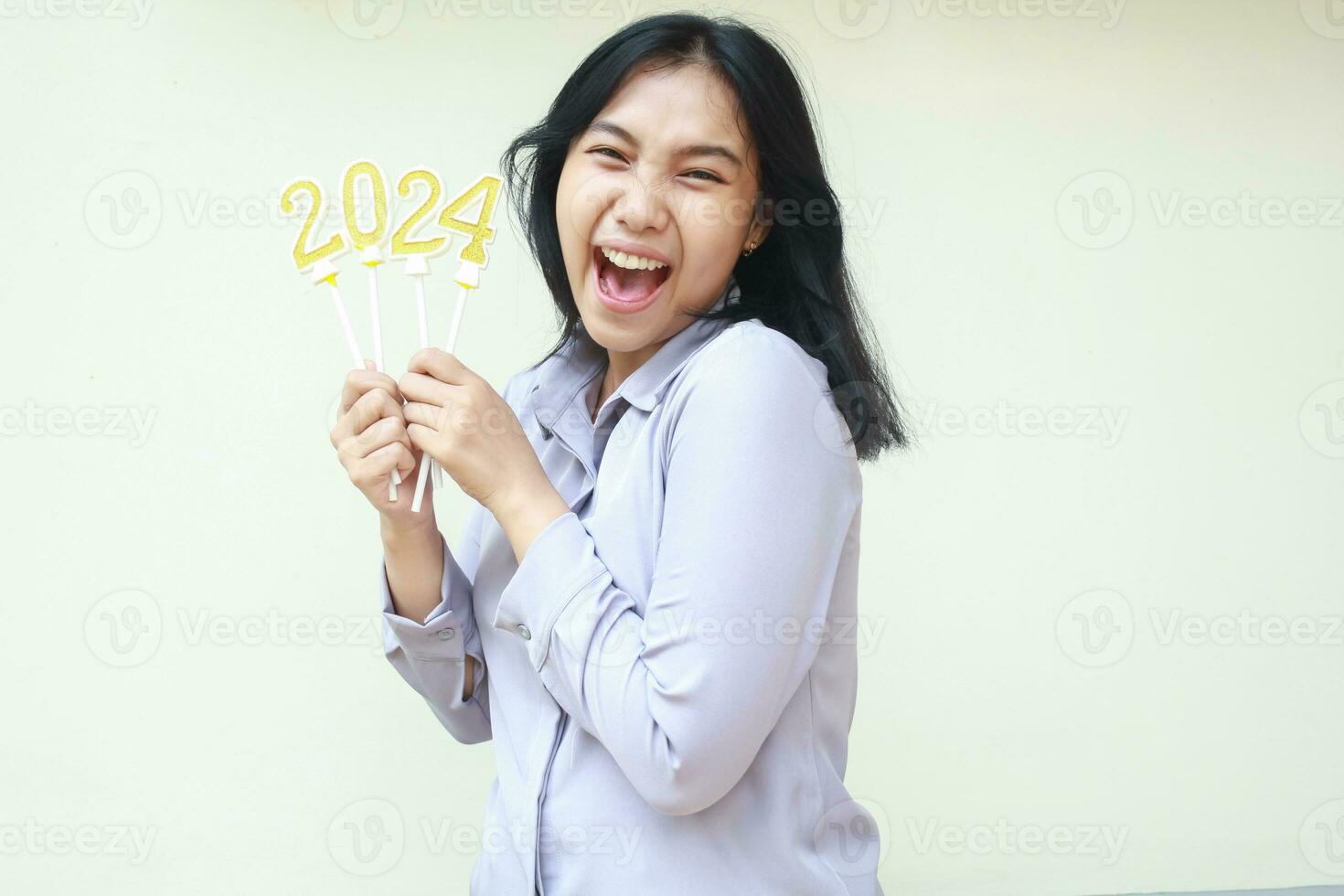 aufgeregt jung Geschäft Frau asiatisch schreiend mit öffnen Mund zu Kamera mit erziehen Arm halten 2024 Nummer Kerze, begeistert weiblich Mitarbeiter tragen grau formal passen zu feiern Neu Jahre Vorabend foto