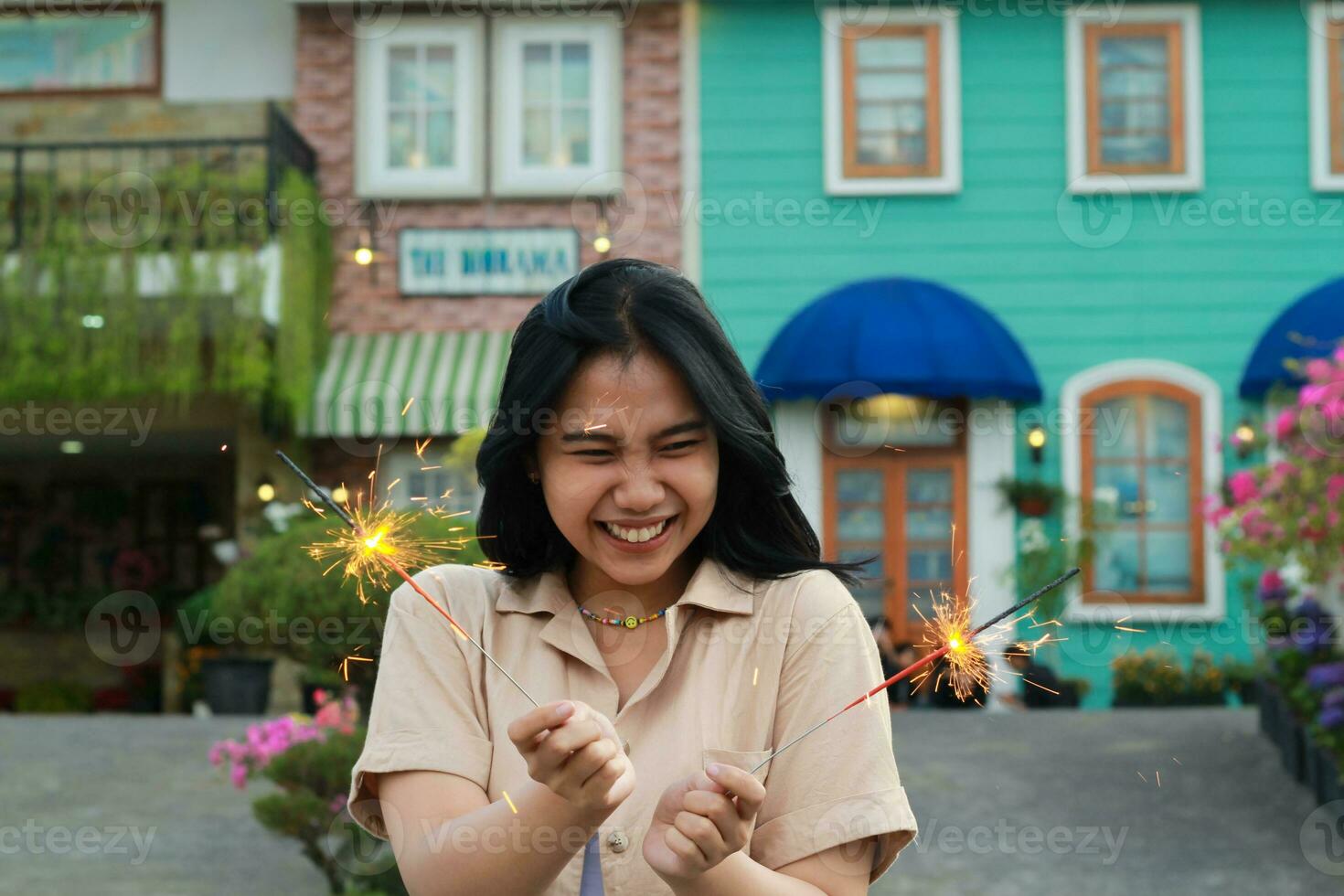 heiter jung asiatisch Frau halten Wunderkerze zu feiern Neu Jahr Vorabend mit Garten Party Stehen Über bunt Jahrgang Haus Hof foto