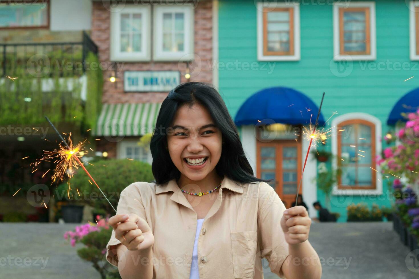 heiter jung asiatisch Frau halten Wunderkerze zu feiern Neu Jahr Vorabend mit Garten Party Stehen Über bunt Jahrgang Haus Hof foto