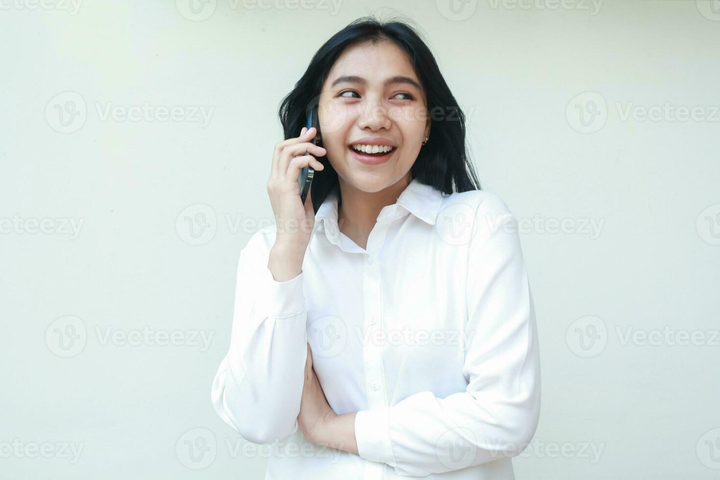 Porträt von sorglos asiatisch jung Frau Exekutive Sprechen auf Smartphone mit Aufregung Gesicht Ausdruck Waffen gefaltet suchen Weg tragen Weiß formal passen Shirt, Stehen isoliert foto