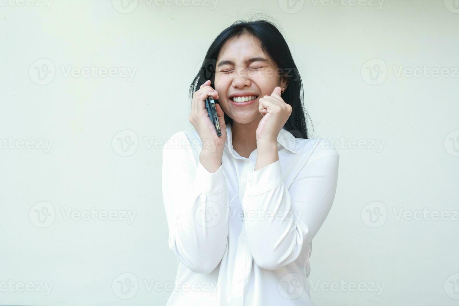 begeistert schön asiatisch Geschäft Frau Unternehmer Lachen mit geschlossen Auge während Sprechen auf Handy, Mobiltelefon Telefon und erziehen Palmen tragen Weiß formal passen Shirt, feiern gewinnen Sieg, Stehen foto