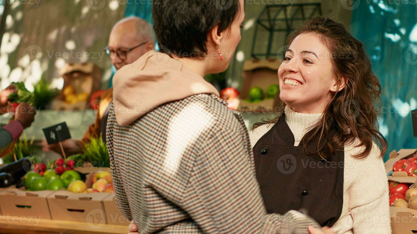 heiter Verkäufer umarmen und Gruß regulär Klient, Gefühl glücklich beim lokal Essen Marktplatz. jung Frauen Teilen Umarmung beim Bauern Markt, genießen Besuch von treu Kunde. Handheld Schuss. foto