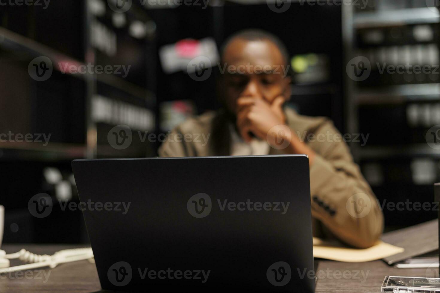 Detektiv Dirigieren Ermittlung mit Laptop im dunkel Büro. erschöpft überarbeitet Polizist suchen Einblick zum lösen Verbrechen mit tragbar Computer schließen oben selektiv Fokus foto