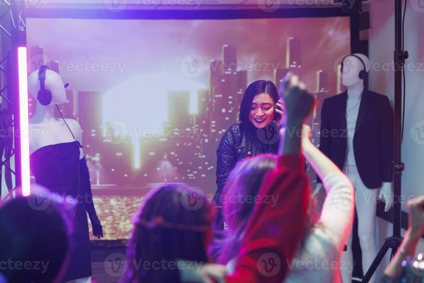 Menschen Teilnahme Techno Musik- Konzert im Nachtclub während asiatisch dj durchführen. Frau Musiker halten Kopfhörer während Mischen Klang mit Regler während Party im Nachtclub foto