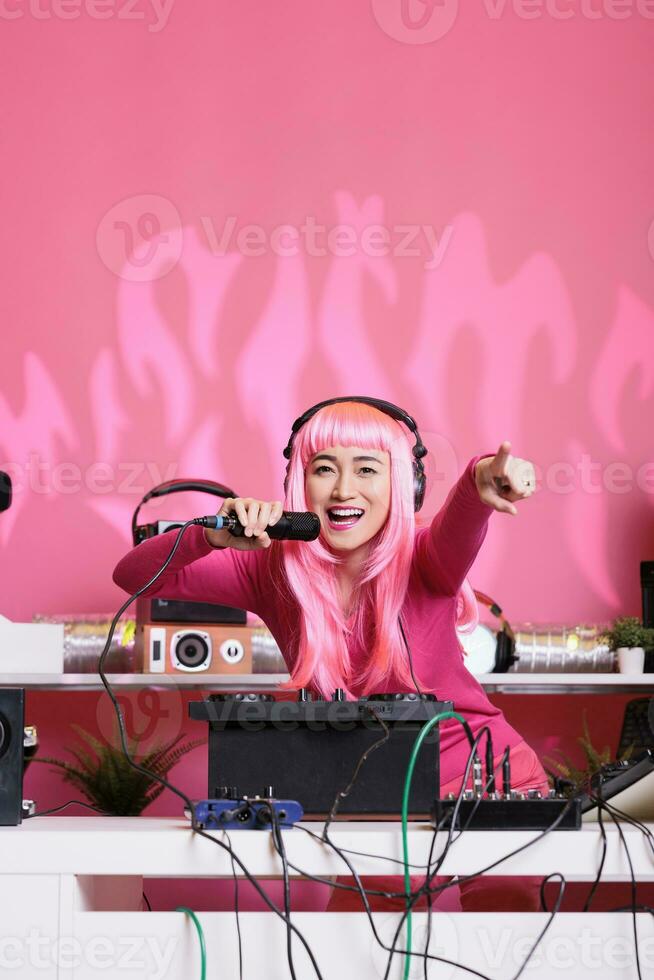 Frau Künstler Sitzung beim dj Tabelle durchführen Techno Musik- mit Fachmann Rührgerät Konsole, tragen Headset und reden mit Fans mit Mikrofon. asiatisch Künstler spielen elektronisch Lied beim Nacht foto