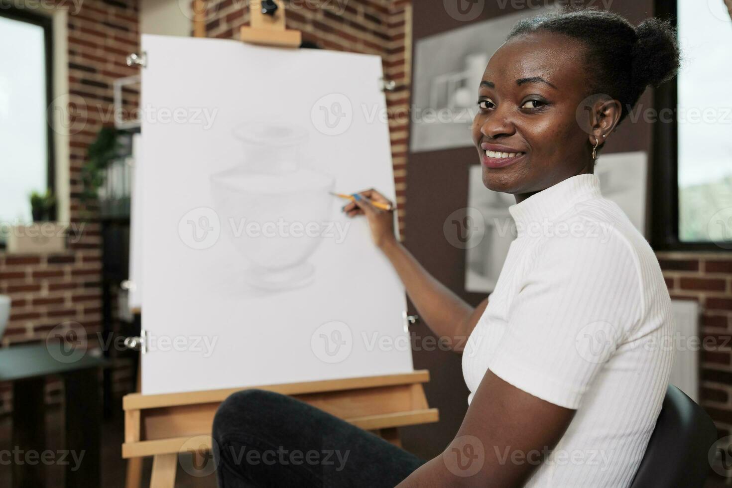 glücklich inspiriert jung afrikanisch amerikanisch Frau Erstellen einzigartig Stück von Kunst während kreativ Kunst Werkstatt, Sitzung beim Staffelei und lächelnd beim Kamera, genießen Zeichnung Lektion, Entwicklung ihr besitzen Kreativität foto
