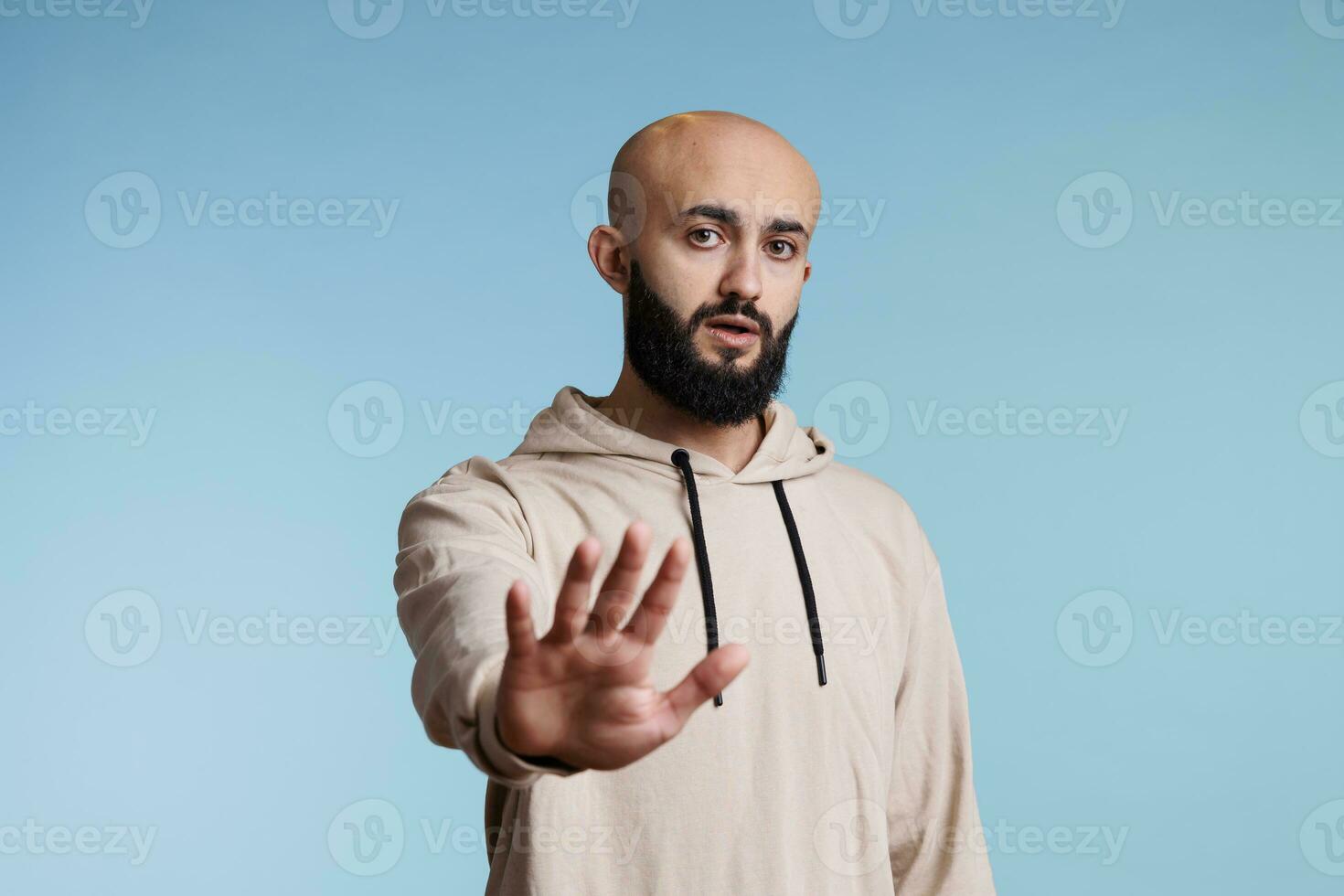 zuversichtlich arabisch Mann Herstellung halt Geste mit Hand, ausdrücken Ablehnung Porträt. jung Person im beiläufig Kapuzenpullover zeigen Nein Signal mit Palme und suchen beim Kamera mit ernst Emotionen foto