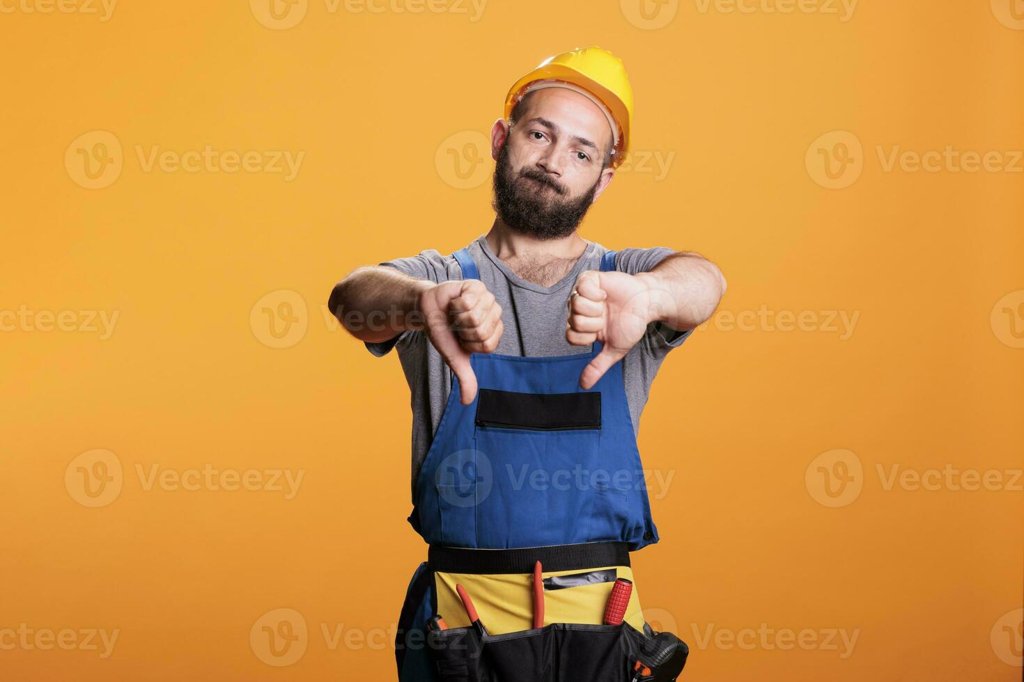 unzufrieden Heimwerker im Overall zeigen Daumen runter, ausdrücken nicht gefallen und Missbilligung Symbol Über Studio Hintergrund. männlich Konstrukteur tun Uneinigkeit Geste, Sein enttäuscht. foto