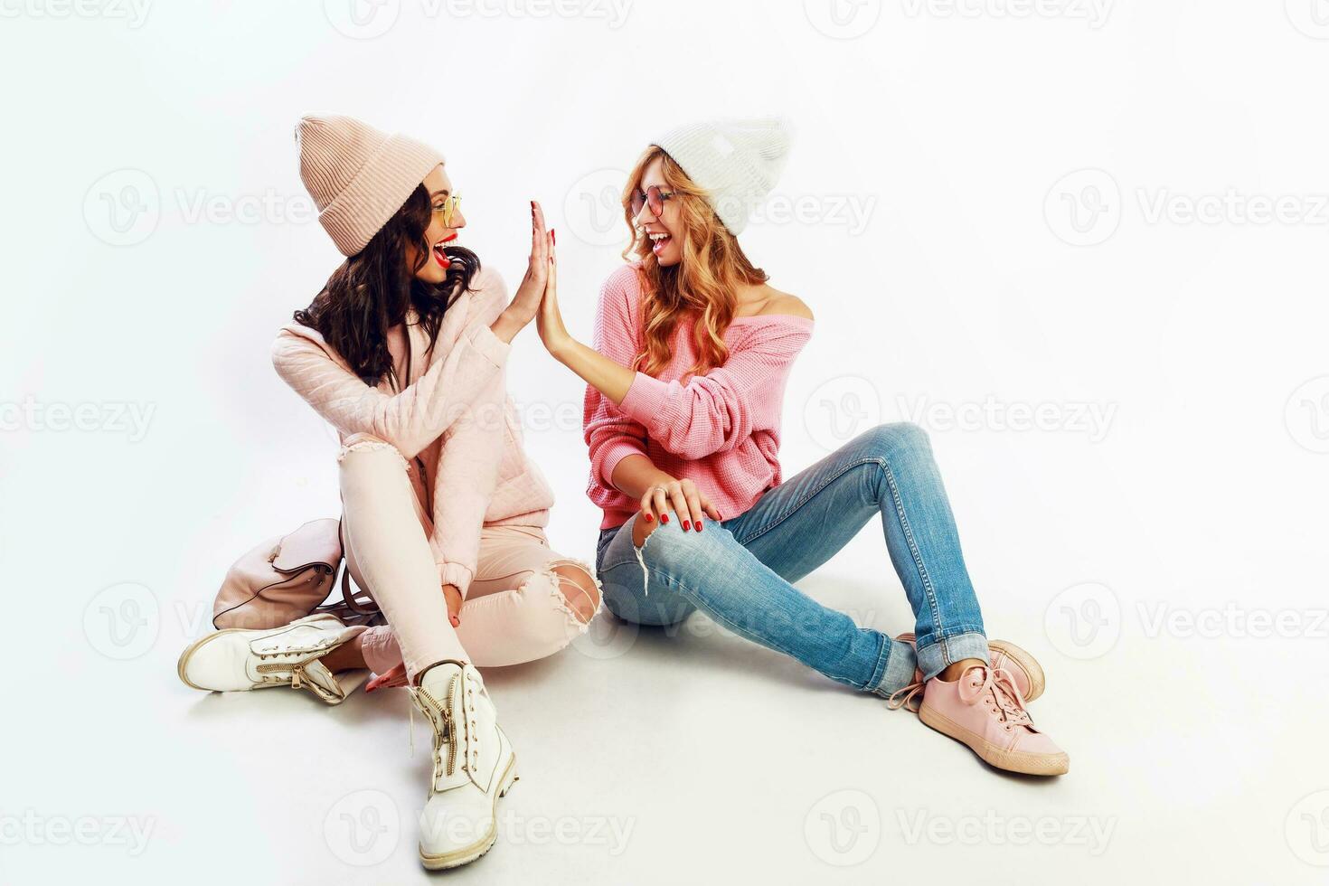 zwei begeistert Frauen im schön Rosa Winter Outfit, Rosa Hüte und Pullover entspannend auf Fußboden , haben Spaß auf Weiß Hintergrund. foto