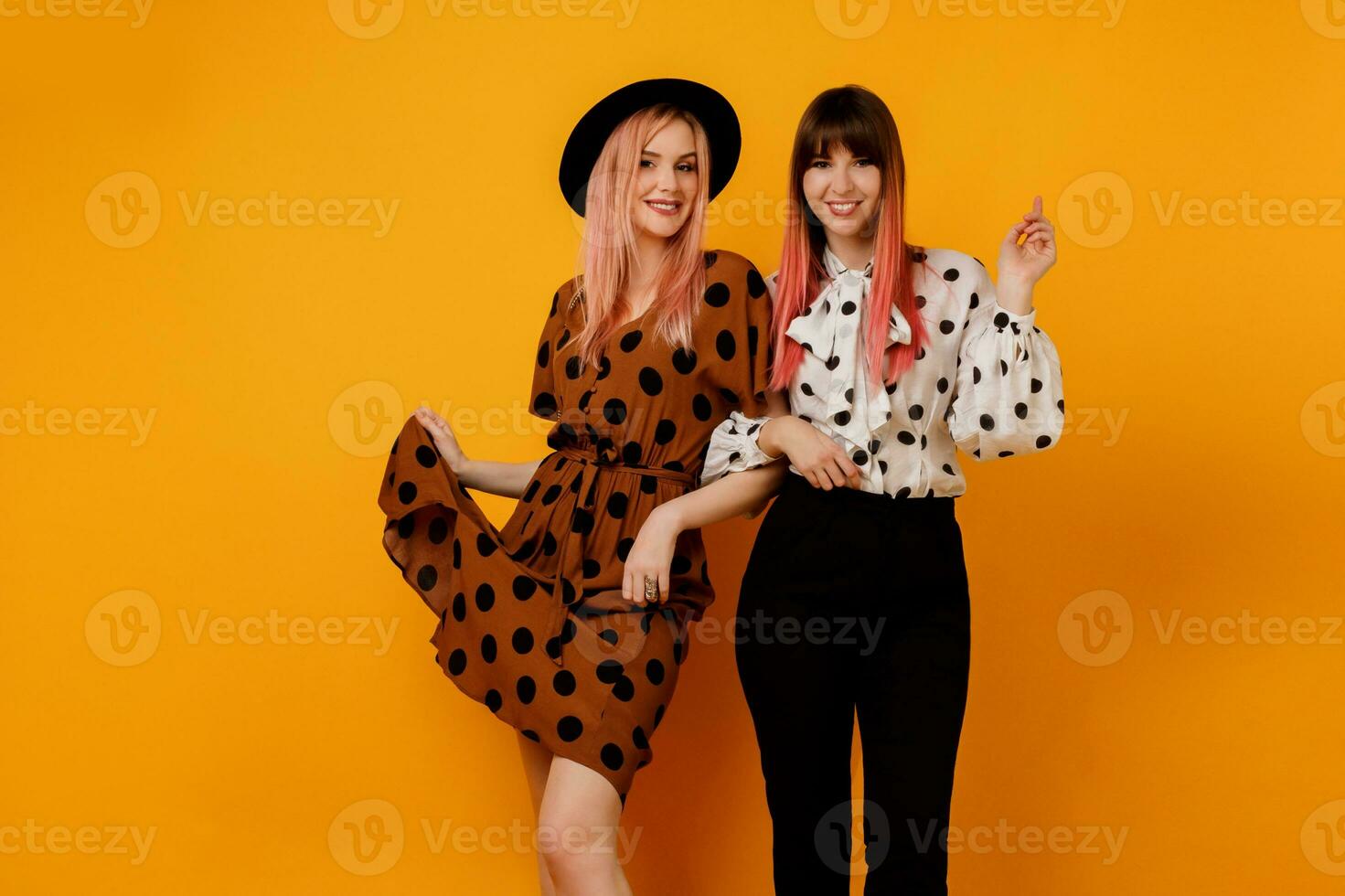 Innen- Studio Bild von zwei stilvoll elegant Frauen im Kleid posieren Über Gelb Hintergrund. froh weiblich Modelle im stilvoll Kleidung. Einkaufen und Mode Konzept. foto