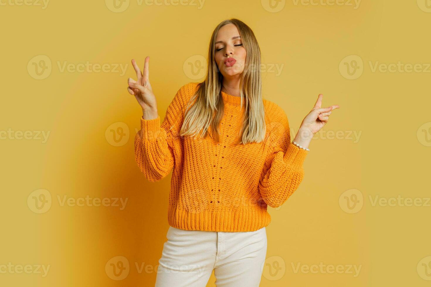 glücklich blond Frau im Orange stilvoll Herbst Sweatshirt posieren Über Gelb Hintergrund im Studio. foto