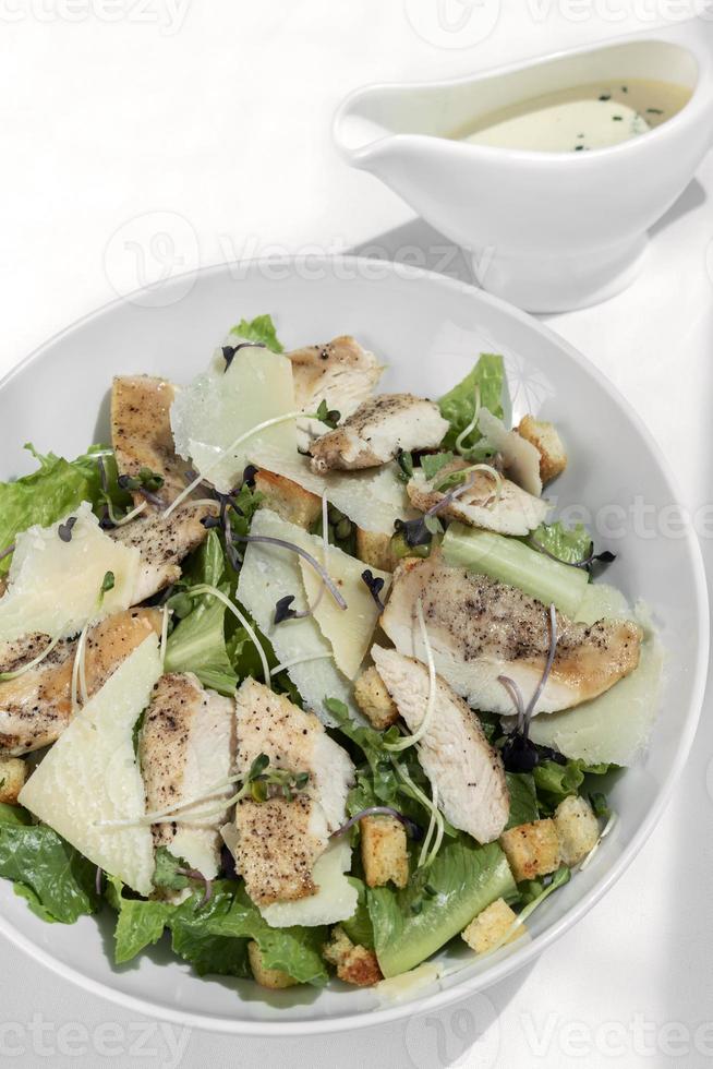 Bio-Hähnchen-Caesar-Salat mit Parmesan und Croutons auf weißem Tischhintergrund foto