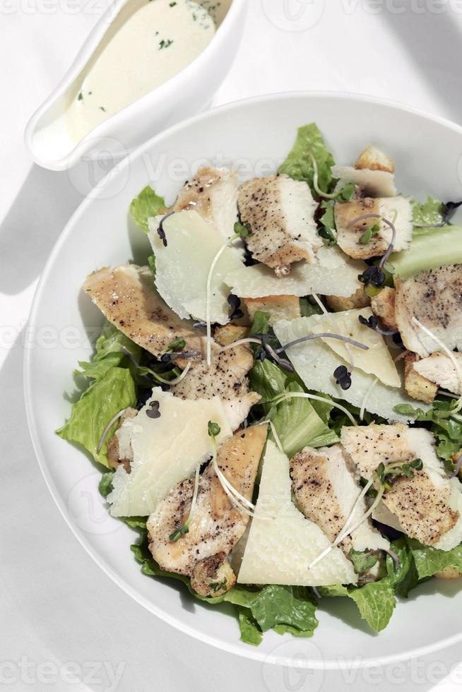 Bio-Hähnchen-Caesar-Salat mit Parmesan und Croutons auf weißem Tischhintergrund foto