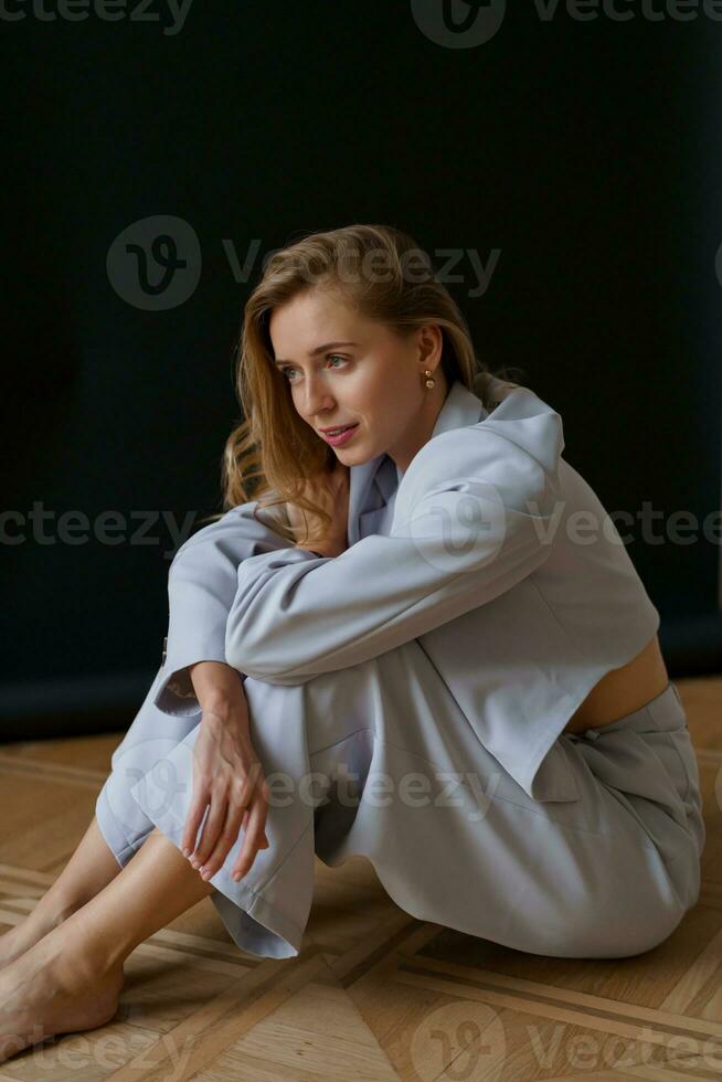 schön verführerisch blond Frau mit wellig Haare im beiläufig elegant Outfit posieren im Studio auf schwarz Hintergrund. Sitzung auf Boden. foto