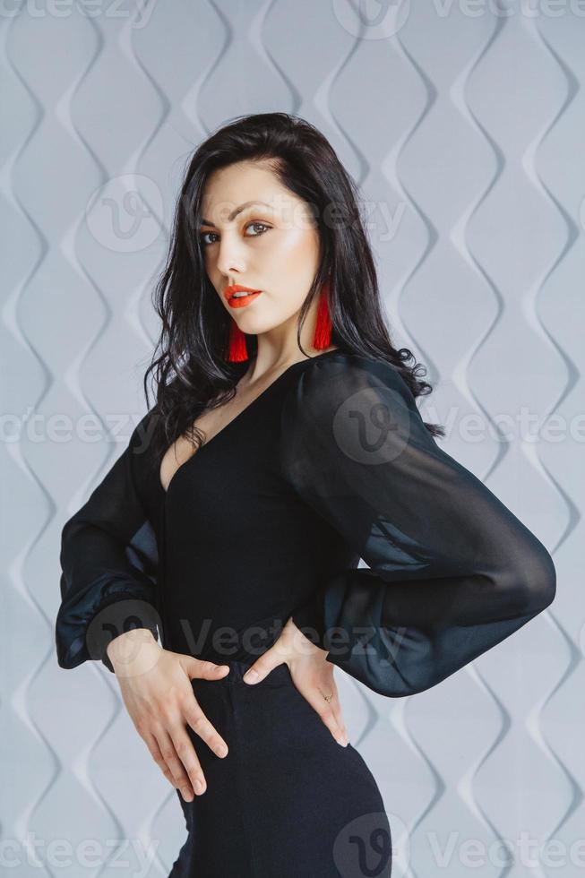 Frau trägt ein schwarzes Kleid, rote Ohrringe im Lichtstudio foto