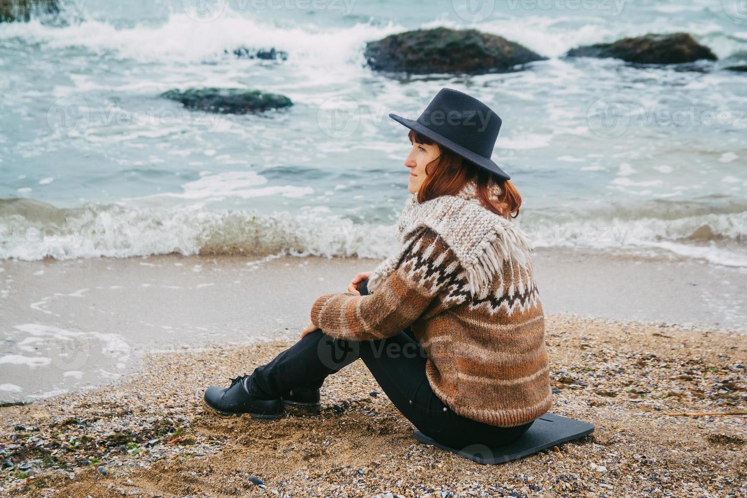 Frau Tourist mit Hut sitzt am Strand mit Blick aufs Meer foto