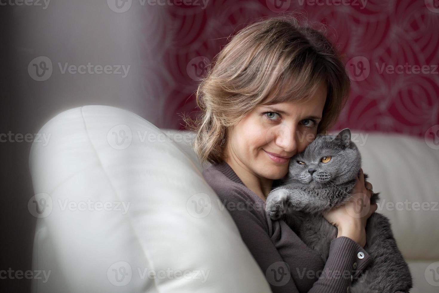 Frau sitzt auf der Couch und streichelt graue Katze foto