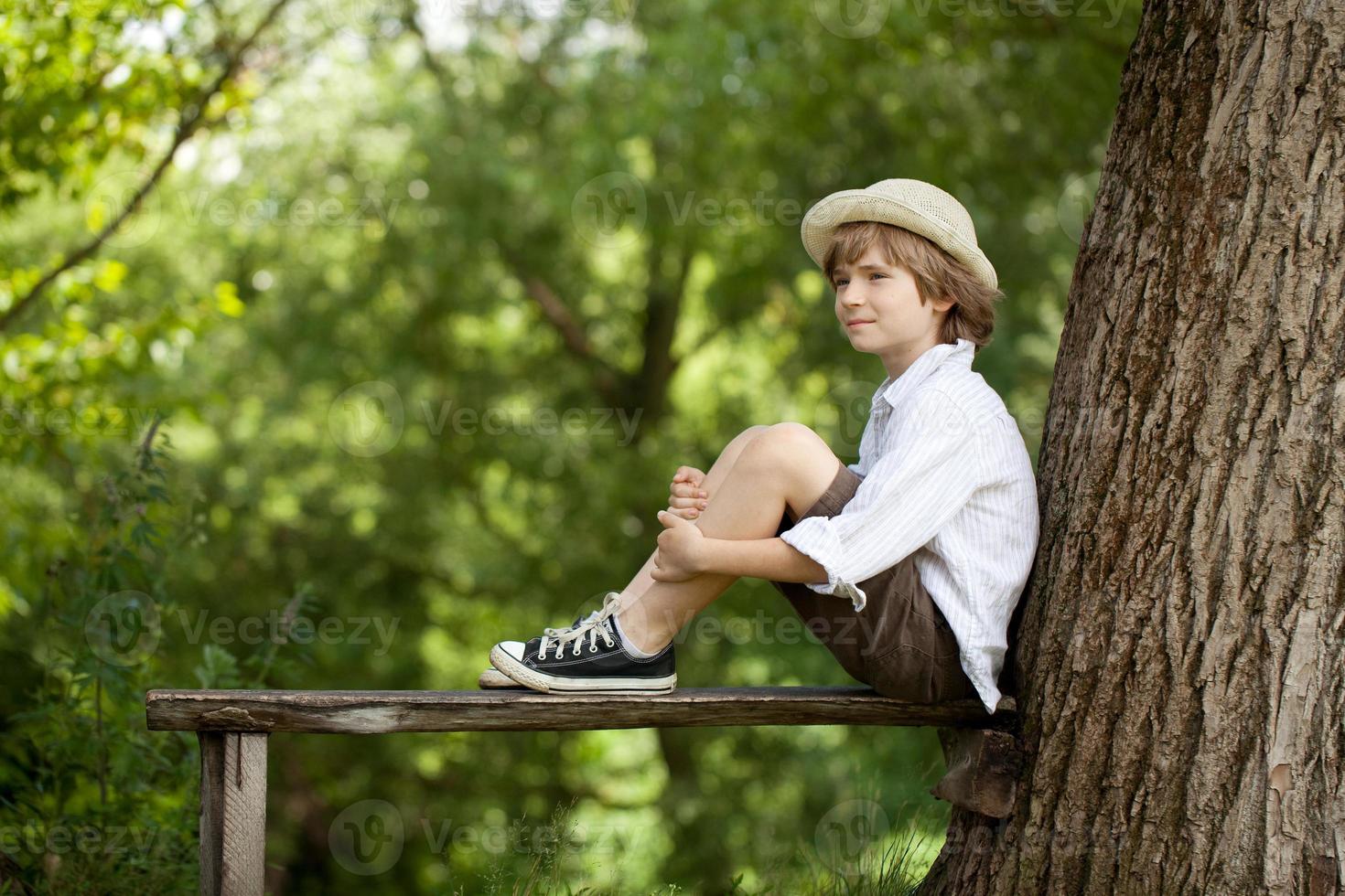Junge sitzt auf einer Holzbank foto
