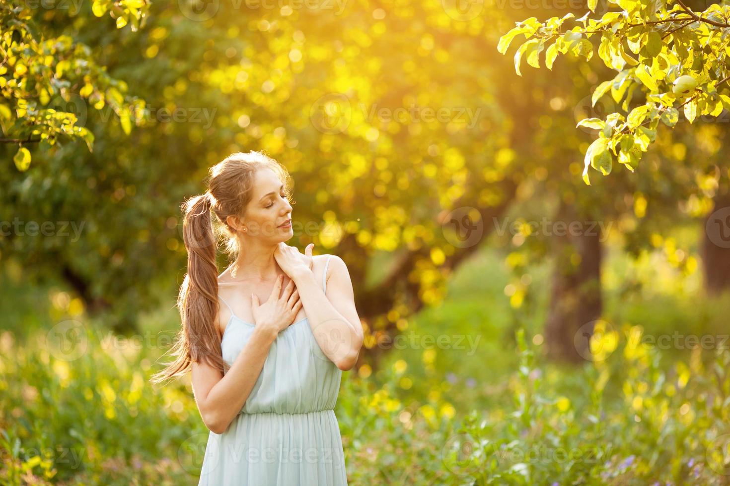 junge glückliche Frau steht mit geschlossenen Augen in einem Garten foto