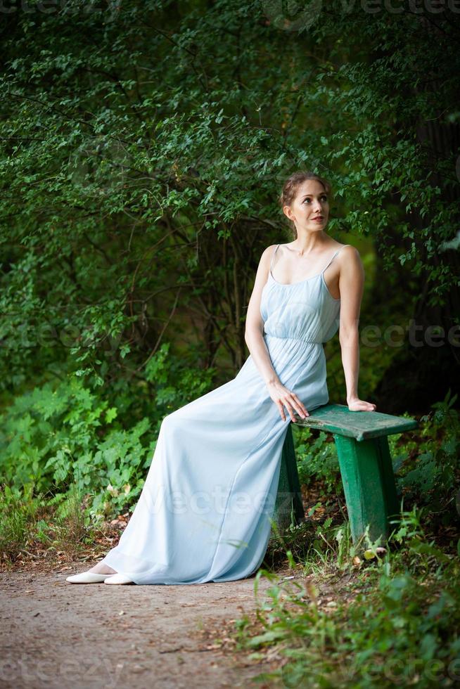 junge Frau in einem Kleid setzte sich auf eine Parkbank foto