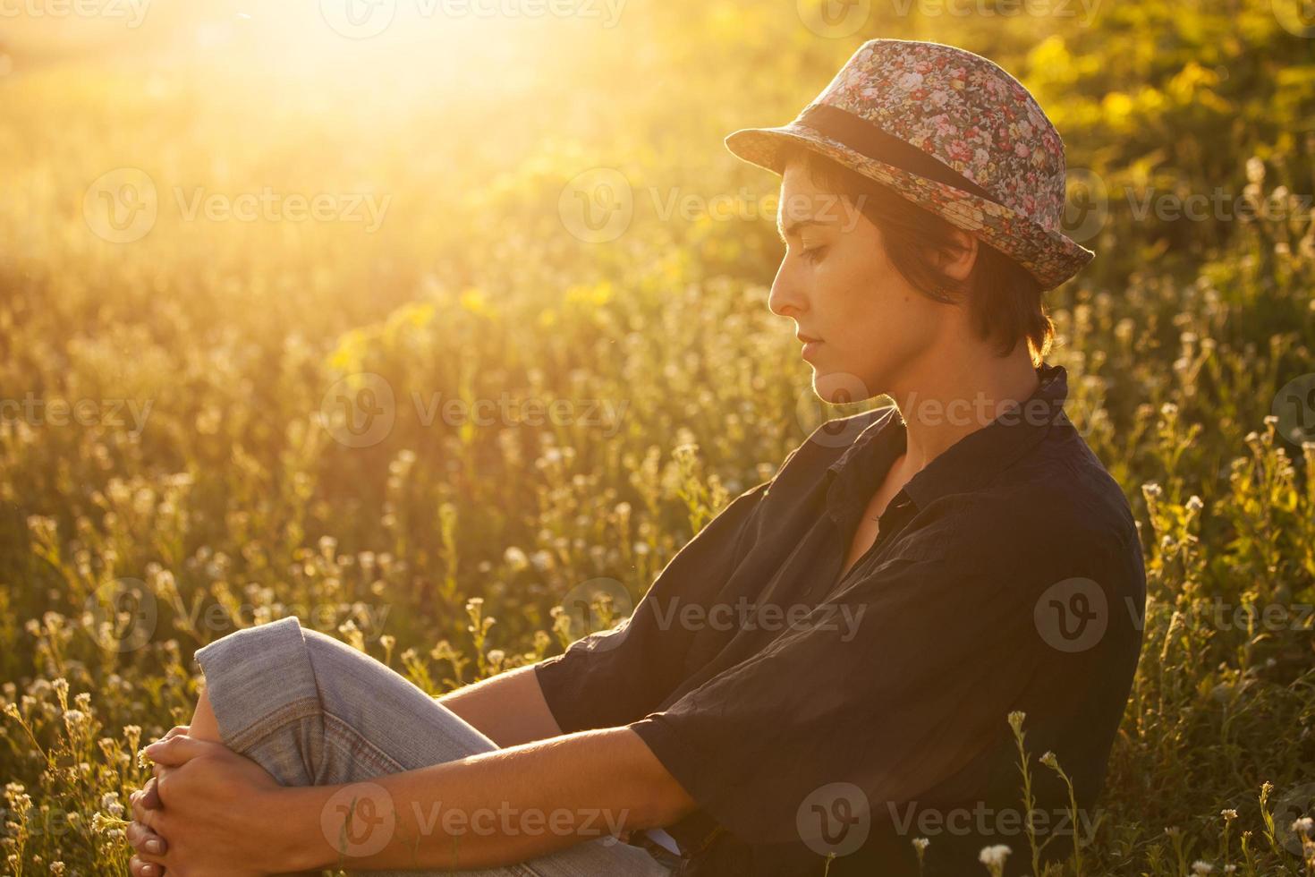 süßes Mädchen, das an einem sonnigen Abend im Gras sitzt foto