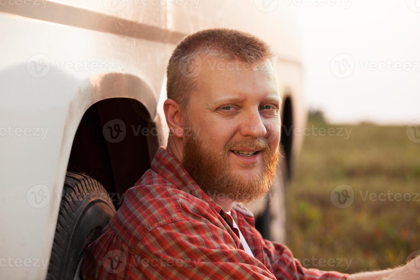 fröhlicher Mann, der in der Nähe des Autos sitzt foto