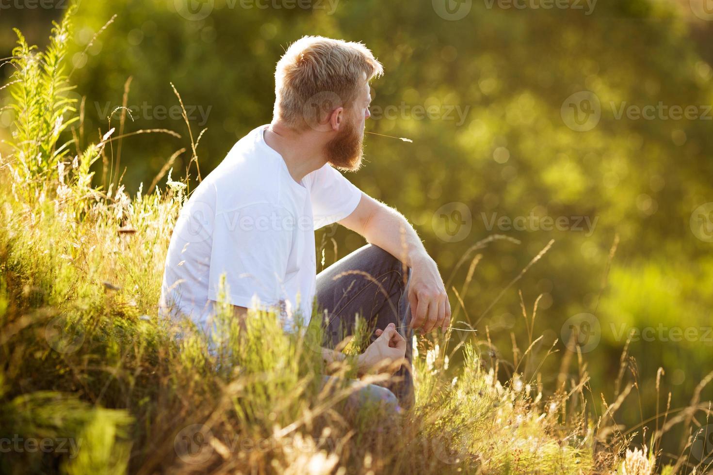 glücklicher Mann, der auf dem Gras sitzt foto