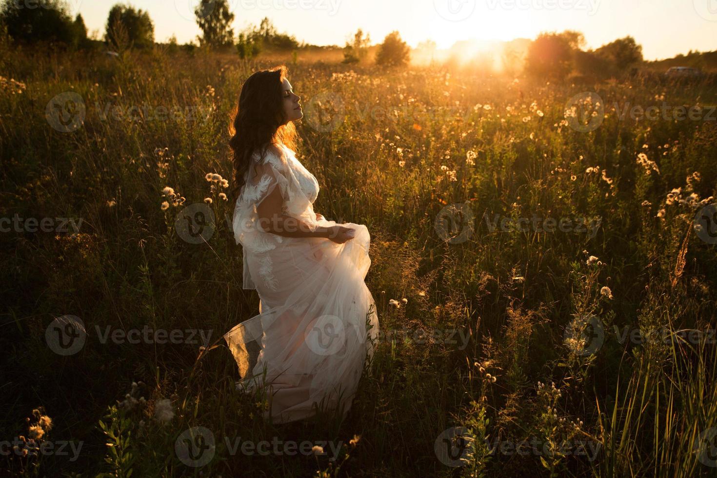 Mädchen in einem Kleid geht abends über das Feld foto