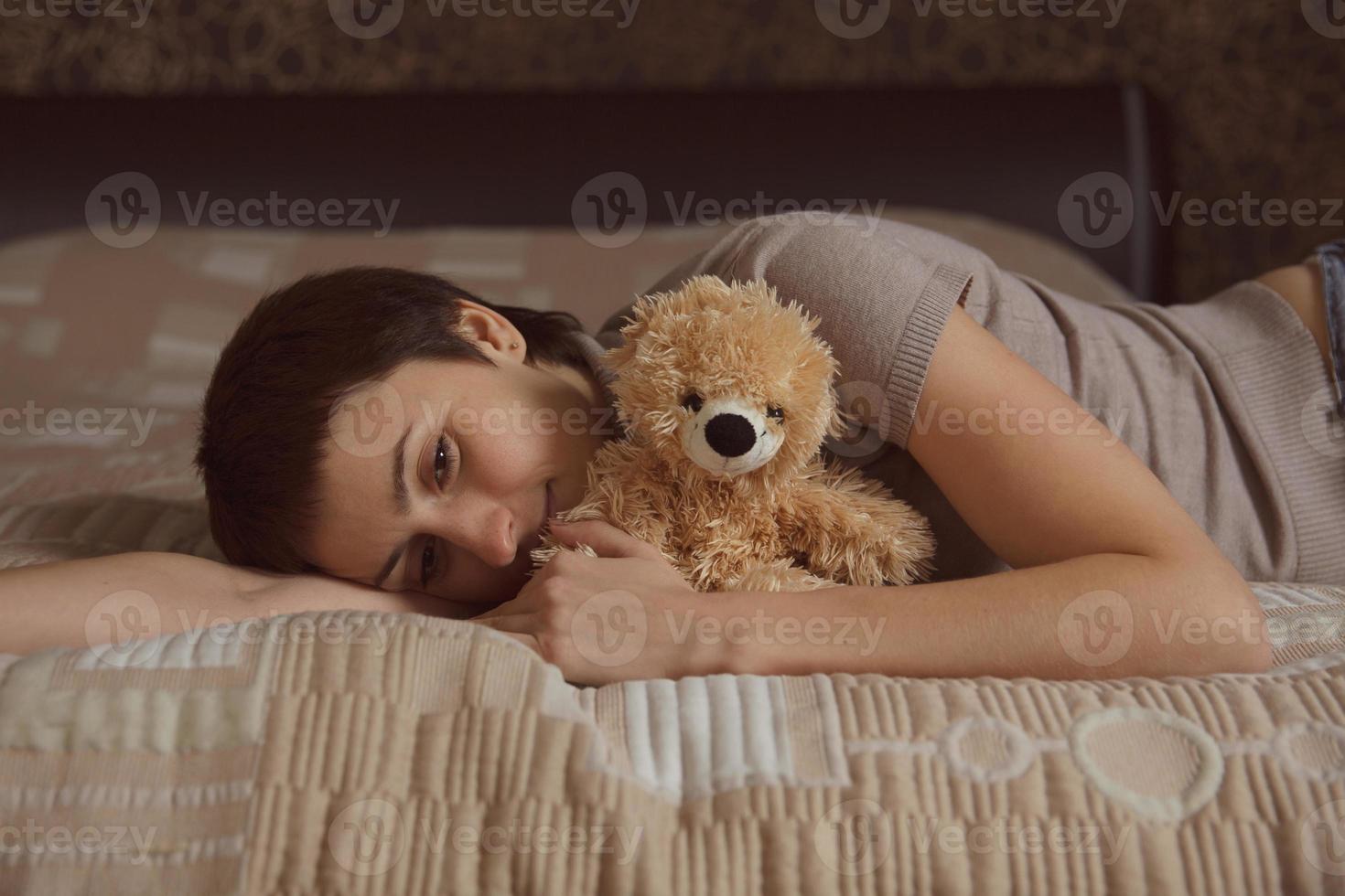 junge Frau liegt mit einem Teddybären auf dem Bett foto