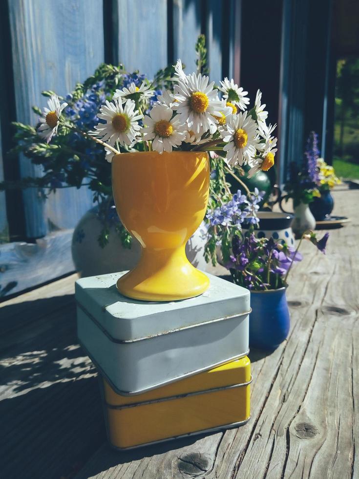 Blumenkomposition aus Gänseblümchenblumen und alten Dosen, auf blauem Holzveranda-Hintergrund, Außen- und Raum, Morgengartenszene, natürliches Licht und Schatten, Tageslicht. buntes Stillleben im rustikalen Stil foto