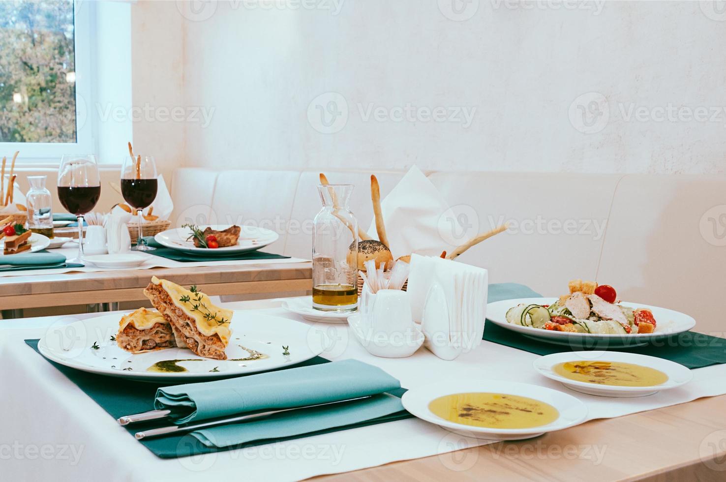 schönes Esszimmer mit Wein- und Wassergläsern, Besteck in grünen Servietten, Essen auf weißen Tellern, arrangiert vom Catering-Service in einem modernen hellen Restaurant, Café. italienische europäische küche foto