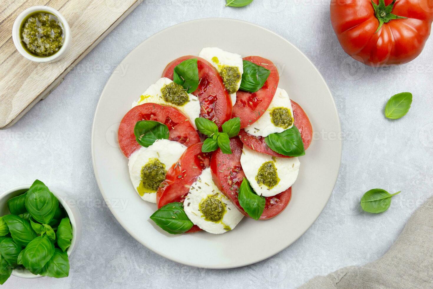 traditionell Italienisch Caprese Salat mit geschnitten Tomaten, Mozzarella, Basilikum, Pesto Soße und würzen auf ein Licht grau Beton Hintergrund. oben Sicht. foto