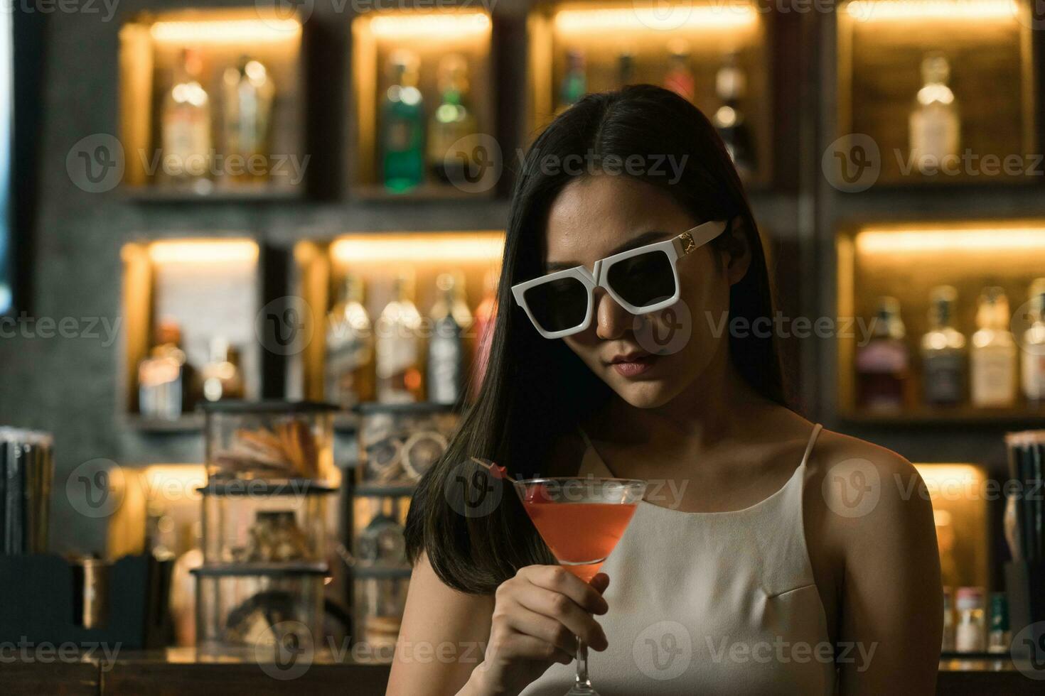 asiatisch Frau Trinken ein Cocktail beim ein Bar während tragen Sonnenbrille. foto