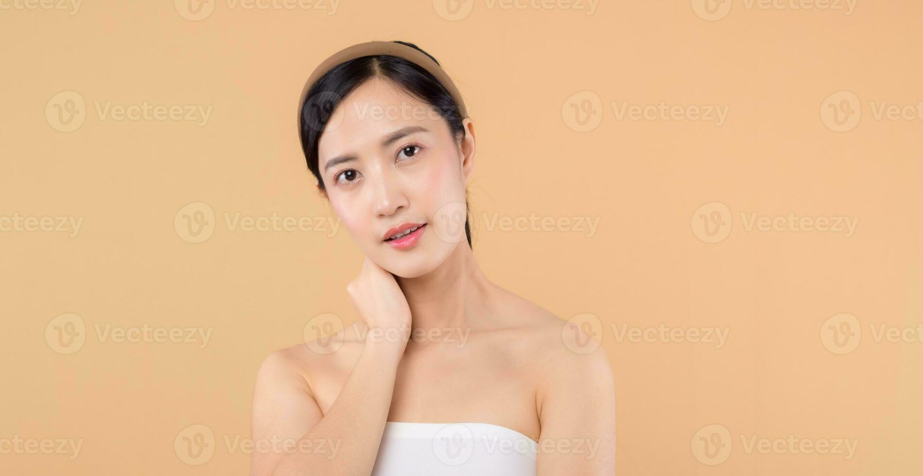 schön Mädchen asiatisch Modell- berühren frisch glühend hydratisiert Gesichts- Haut auf Beige Hintergrund Nahaufnahme. Schönheit Gesicht jung Frau mit natürlich bilden und gesund Haut Porträt. Haut Pflege Konzept foto