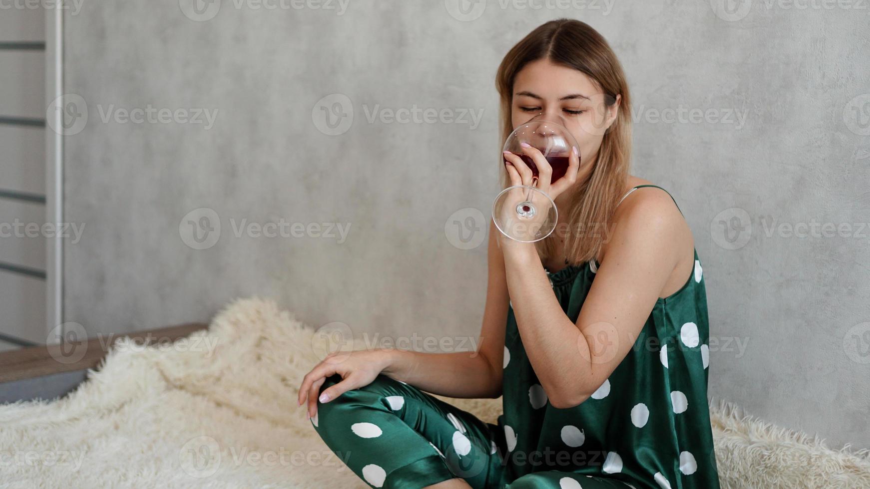 Mädchen im grünen Schlafanzug im Bett mit einem Glas Rotwein foto