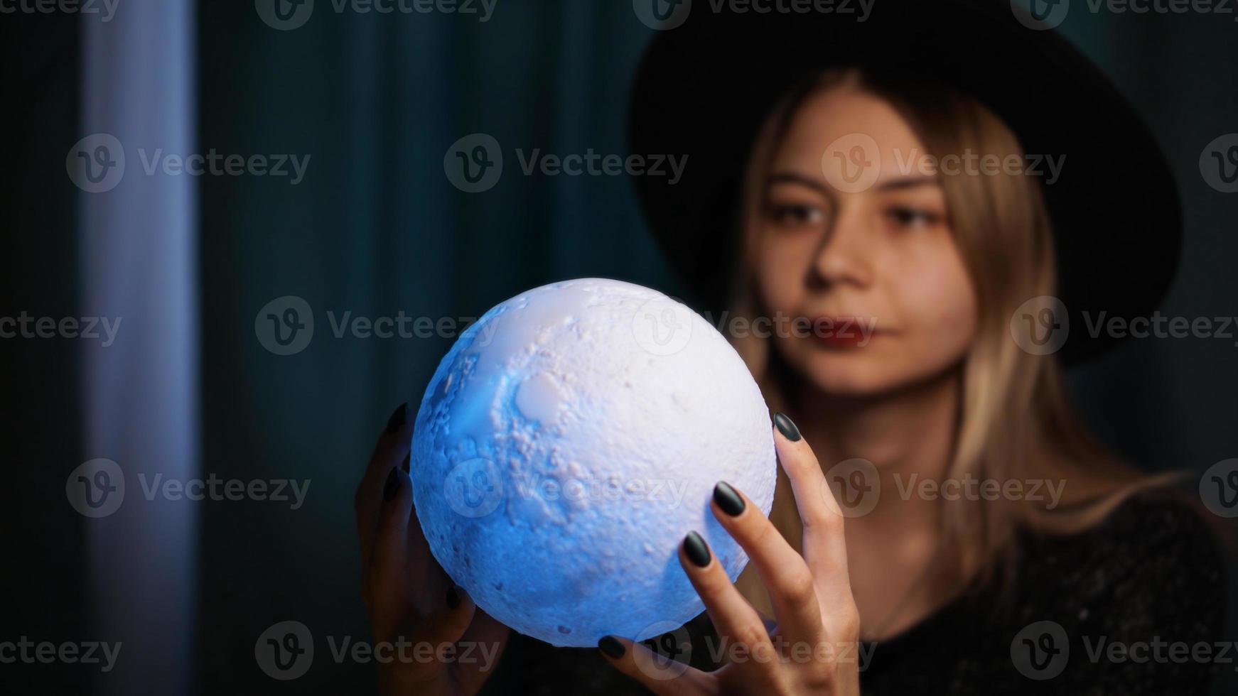 Eine junge Wahrsagerin mit Hut hält einen magischen Ball. foto