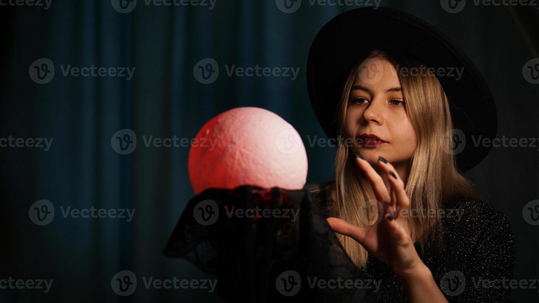 Eine junge Wahrsagerin mit Hut hält einen magischen Ball. foto