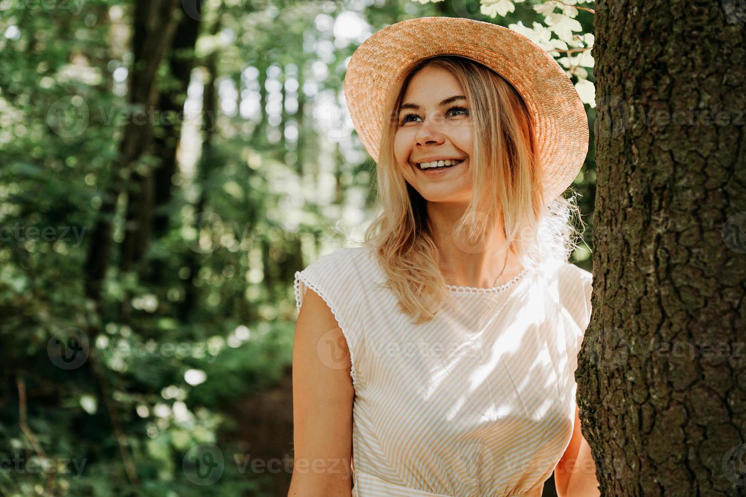 Schönes Mädchen mit Strohhut und stilvoller Kleidung steht in der Nähe eines Baumes foto